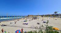 A crowded La Zenia beach with people sitting and standing in the sand.